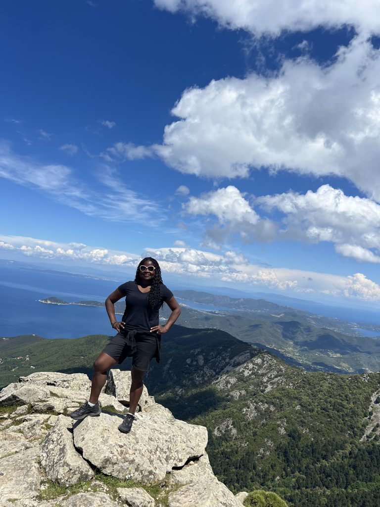 eine Frau steht auf einem Berg zwischen Meer und Himmel